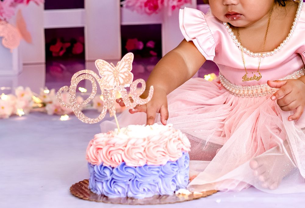 A pink and white decorated smash cake sits ready for a first birthday celebration with matching party decor.