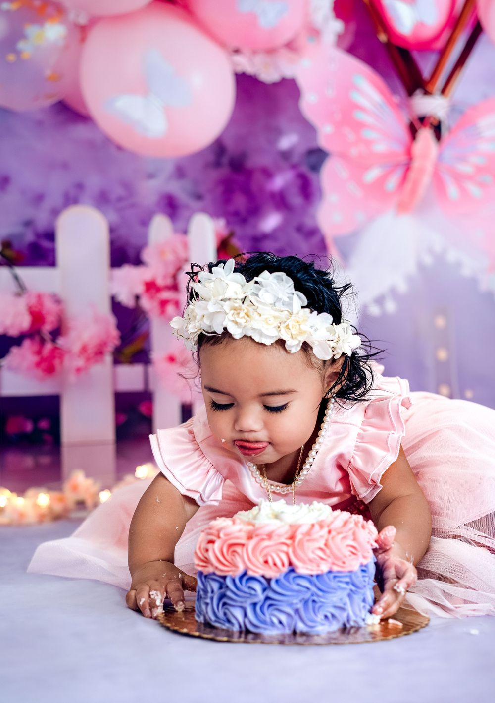 Pink and purple cake smash photo session featuring a small cake with blue and pink frosting decorations.
