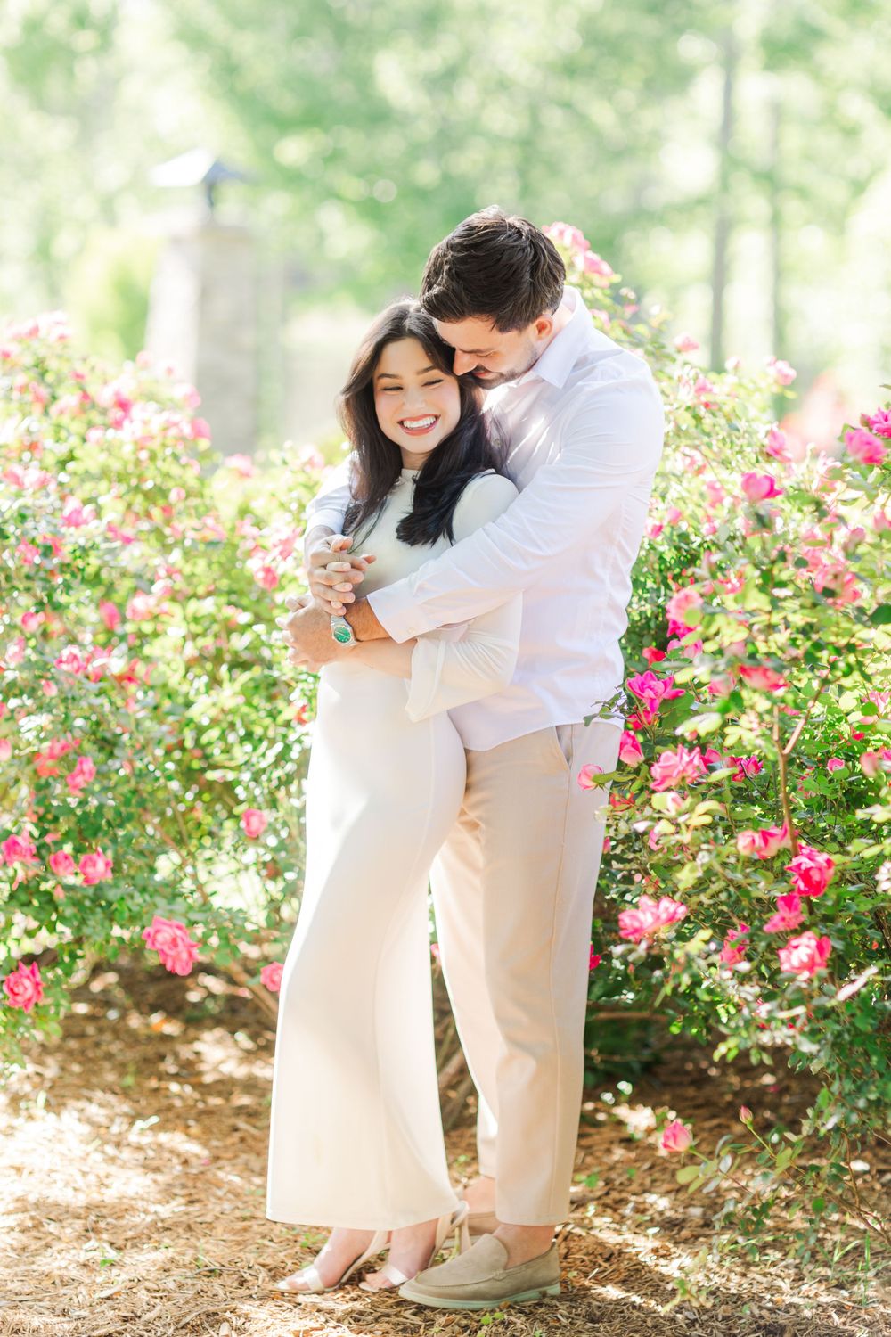 A couple embraces among blooming pink flowers in a garden setting.