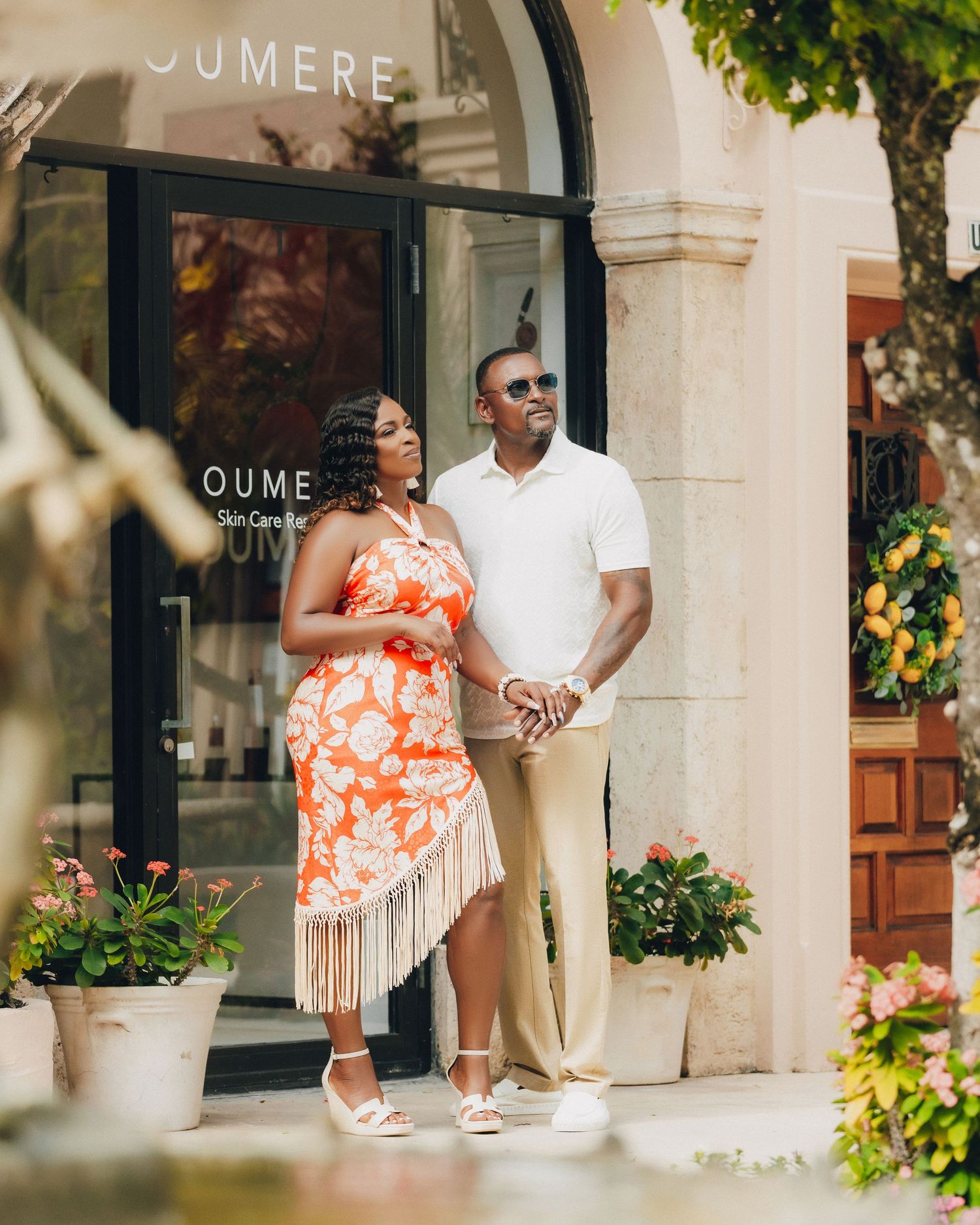 Casual couple posing outside storefront in white shirt and floral fringe dress.