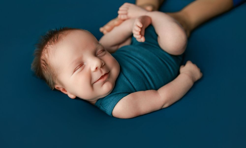 Baby in blue teal colored wrap rests peacefully in multiple artistic angles during newborn photoshoot.