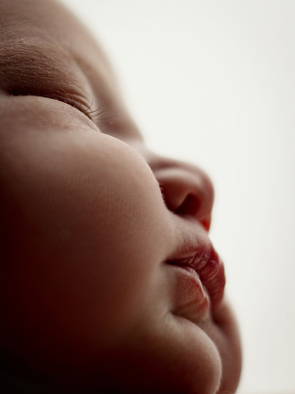Peaceful macro shot of sleeping baby's face showing delicate features in soft lighting.