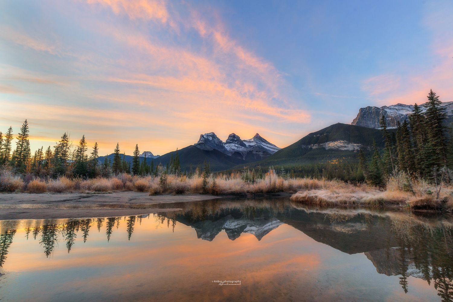 Mountain peaks reflect in calm lake water during colourful sunrise in Canadian Rockies. Canmore - 3 sisters