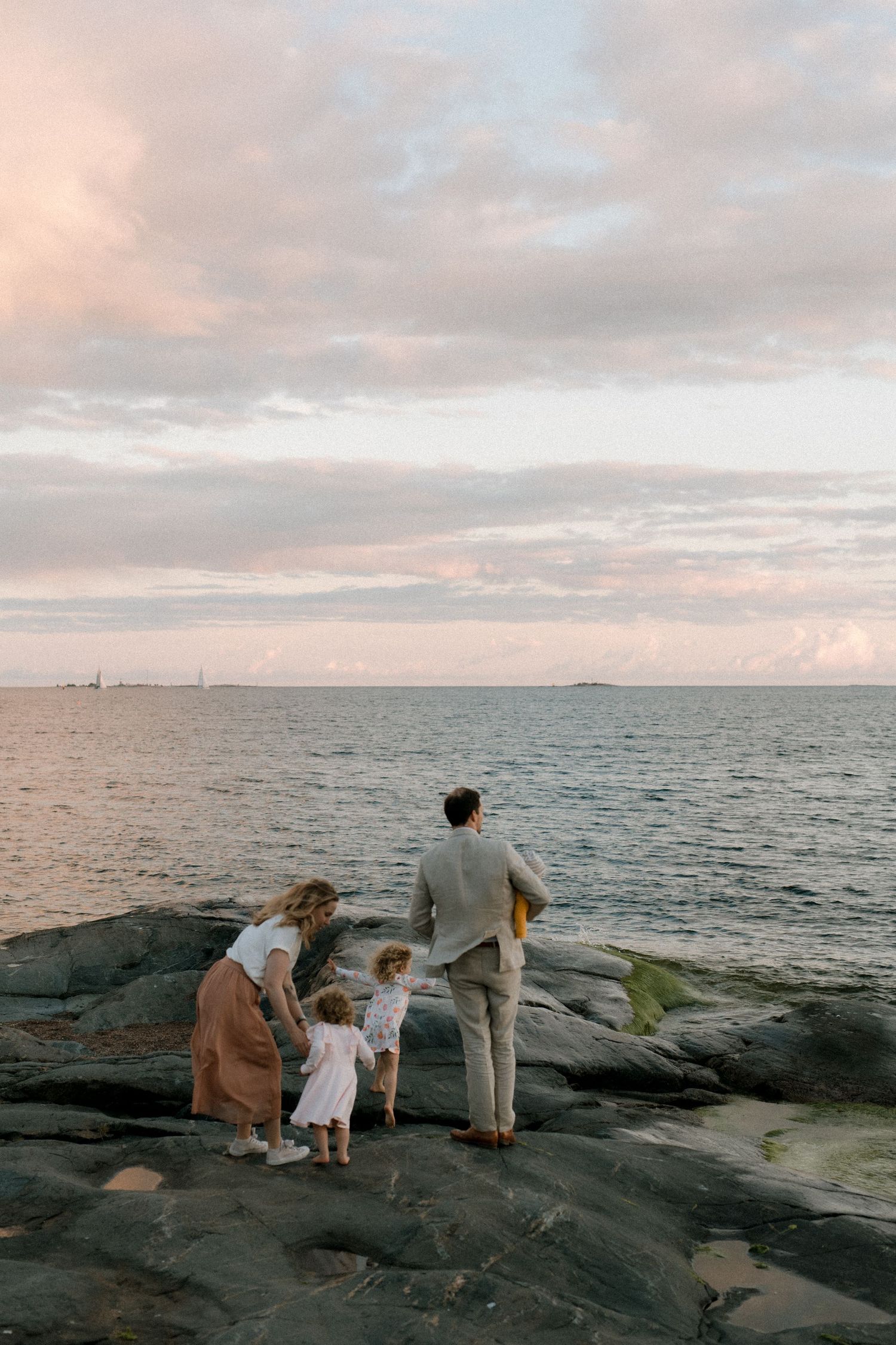 Perhekuva jossa vanhemmat ja kaksi lasta katselevat auringonlaskua rantakalliolla Helsingin Eirassa.