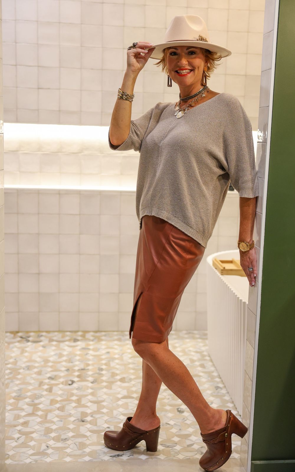 Fashion shoot showing brown leather boots and grey top ensemble against tiled backdrop.