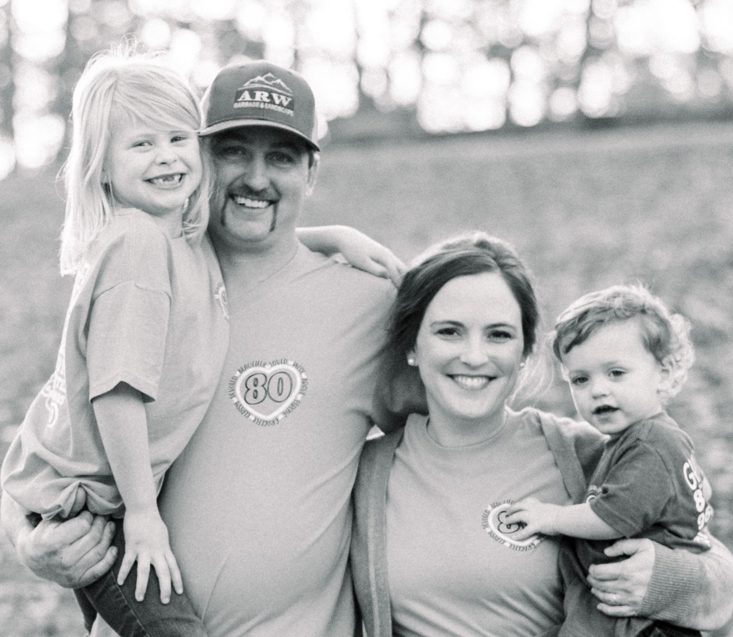 Black and white family portrait of parents and two children wearing matching monogram shirts.