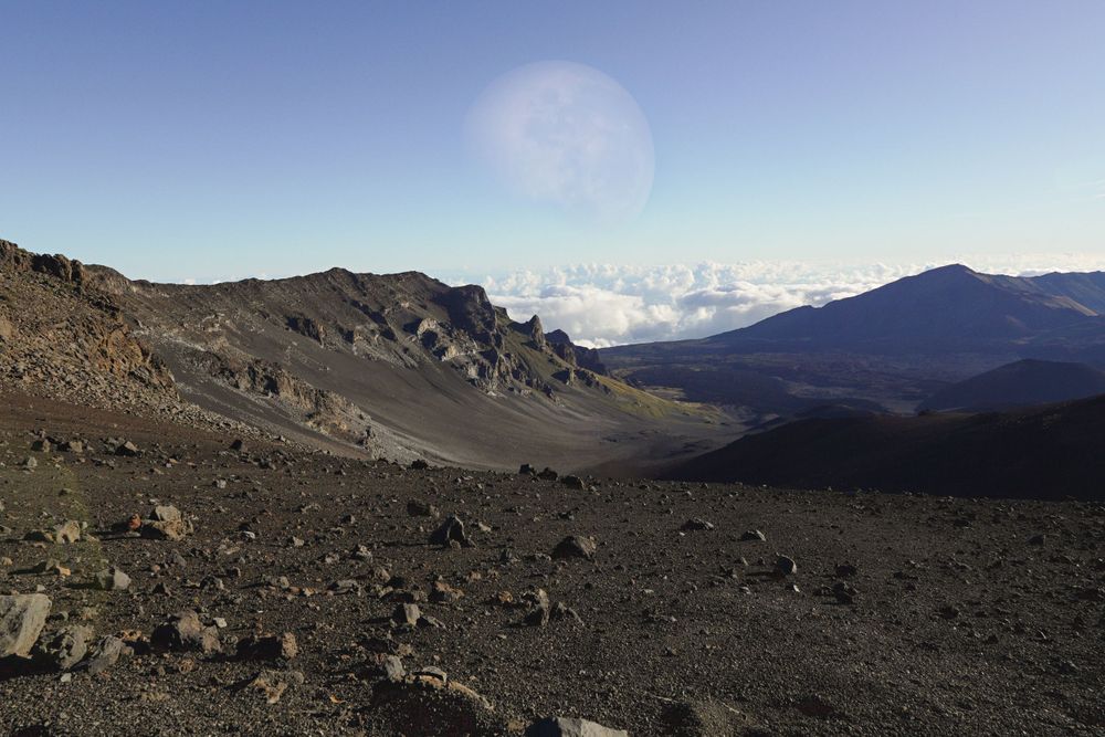 Rugged volcanic mountain terrain with dark rocks and distant peaks against blue sky.