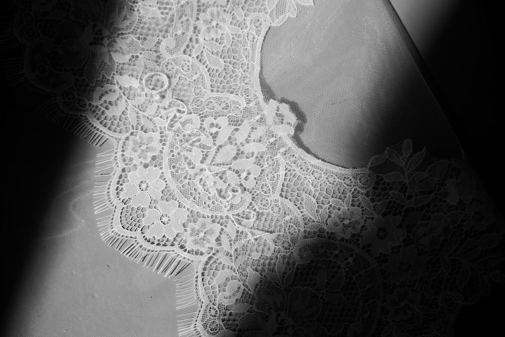 Black and white close-up of intricate floral lace fabric with dramatic light and shadow contrast.