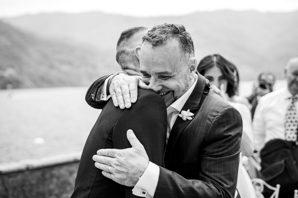 Two people sharing an emotional embrace at an outdoor wedding ceremony with a scenic mountain backdrop.