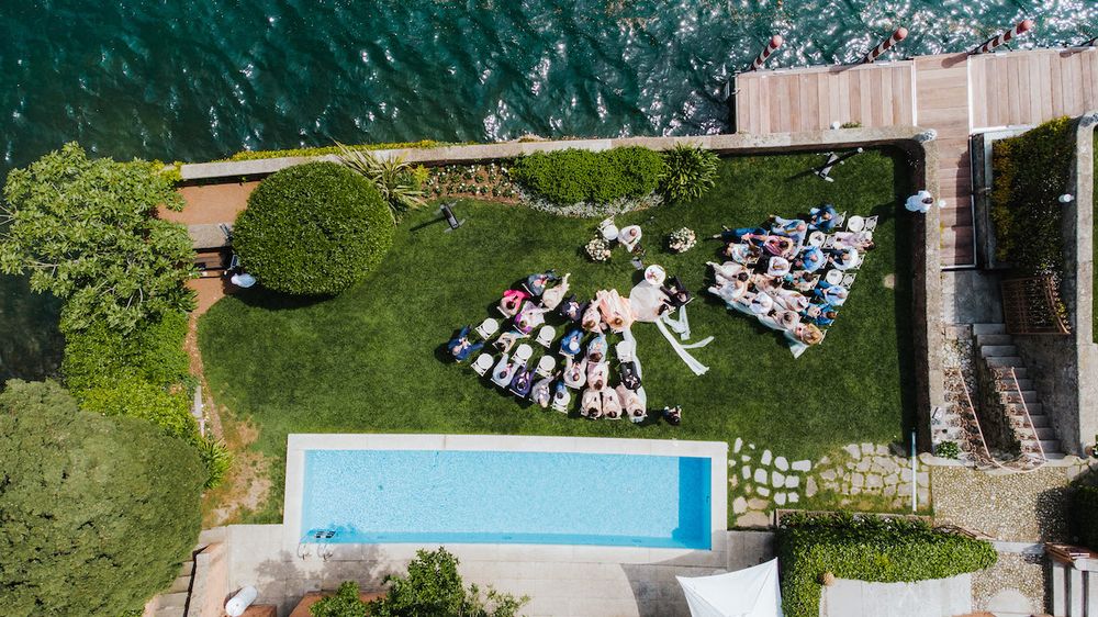 Aerial view of an outdoor wedding reception with pool and scattered guest seating on a manicured lawn.