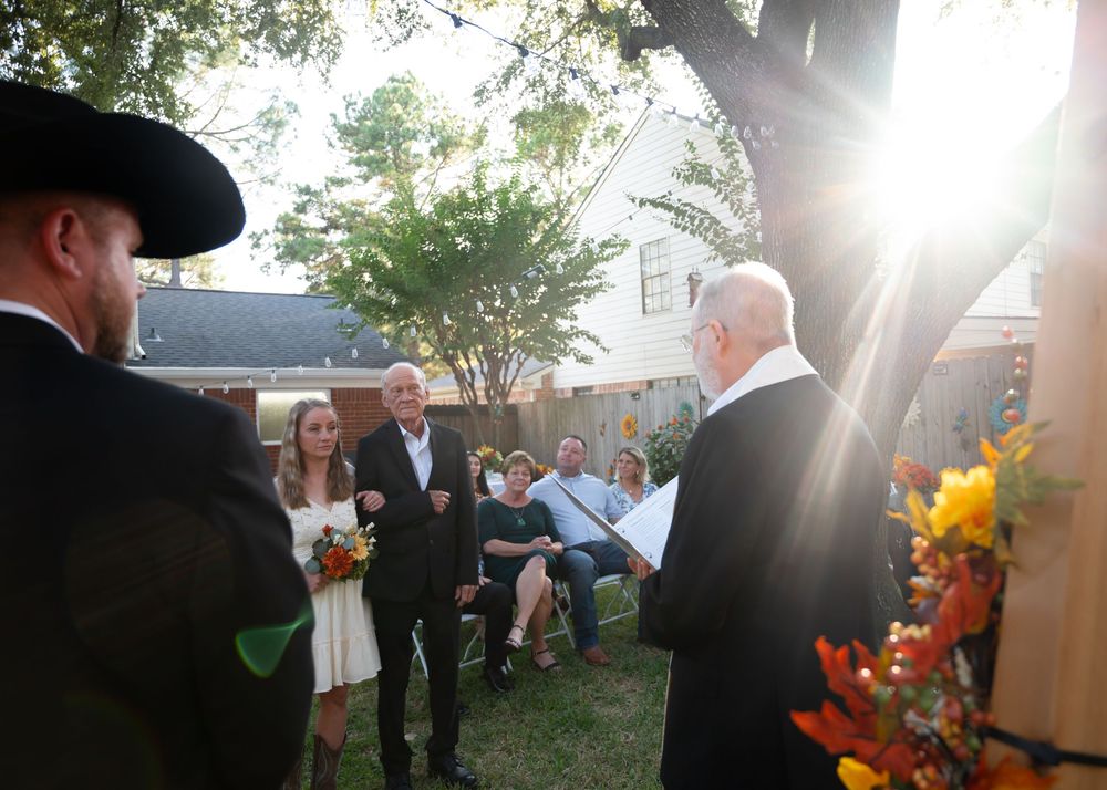 Outdoor backyard wedding ceremony with officiant reading vows in golden sunlight, guests seated behind.