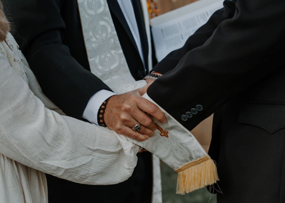 Close-up of wedding ceremony hands joined with officiant stole and bridal party rings.