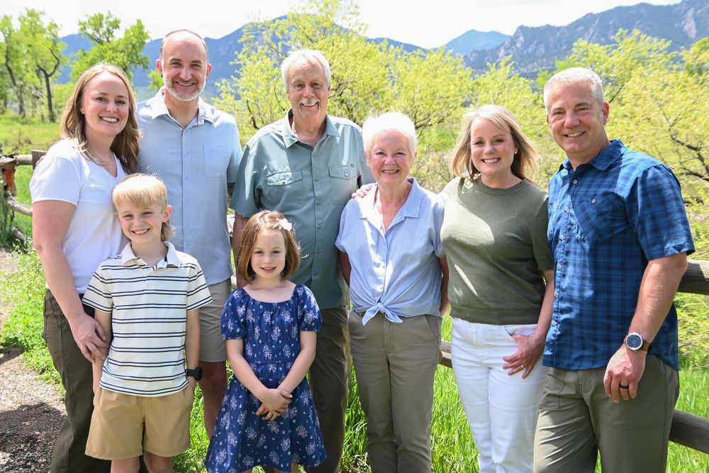 Multi-generational group smiles together outdoors with scenic mountain landscape and greenery in background.