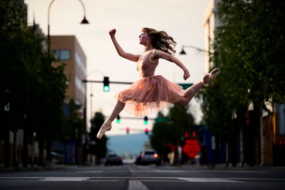 A dancer in a pink tulle dress leaps gracefully across an empty city street at dusk.
