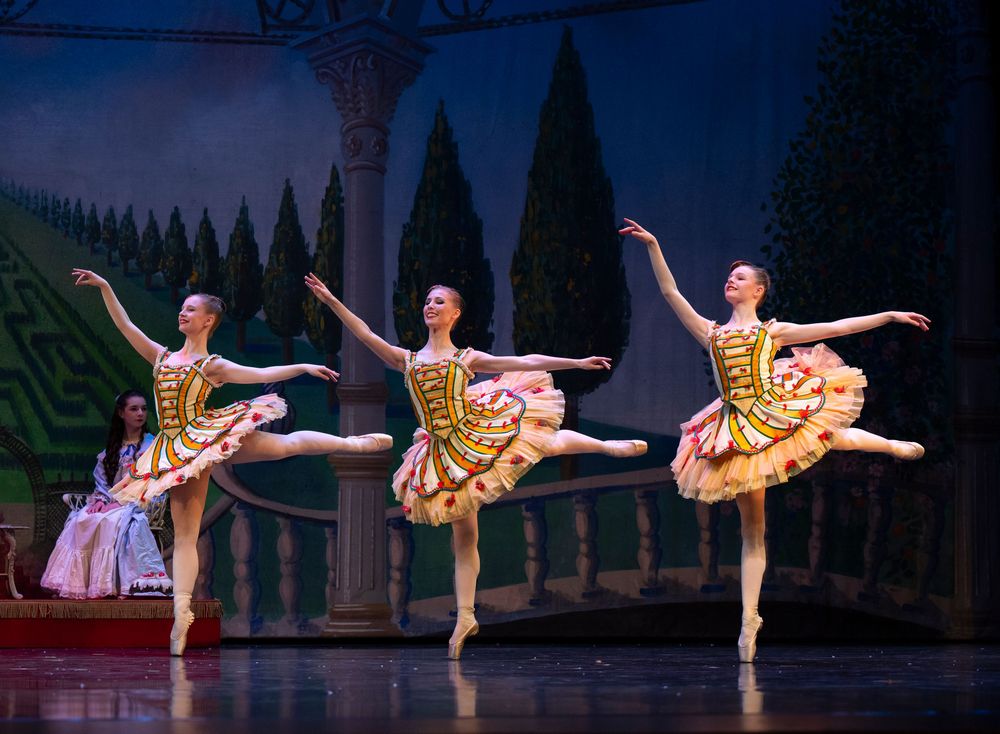 Ballet dancers in yellow and gold tutus perform synchronized leaps during a classical stage performance.
