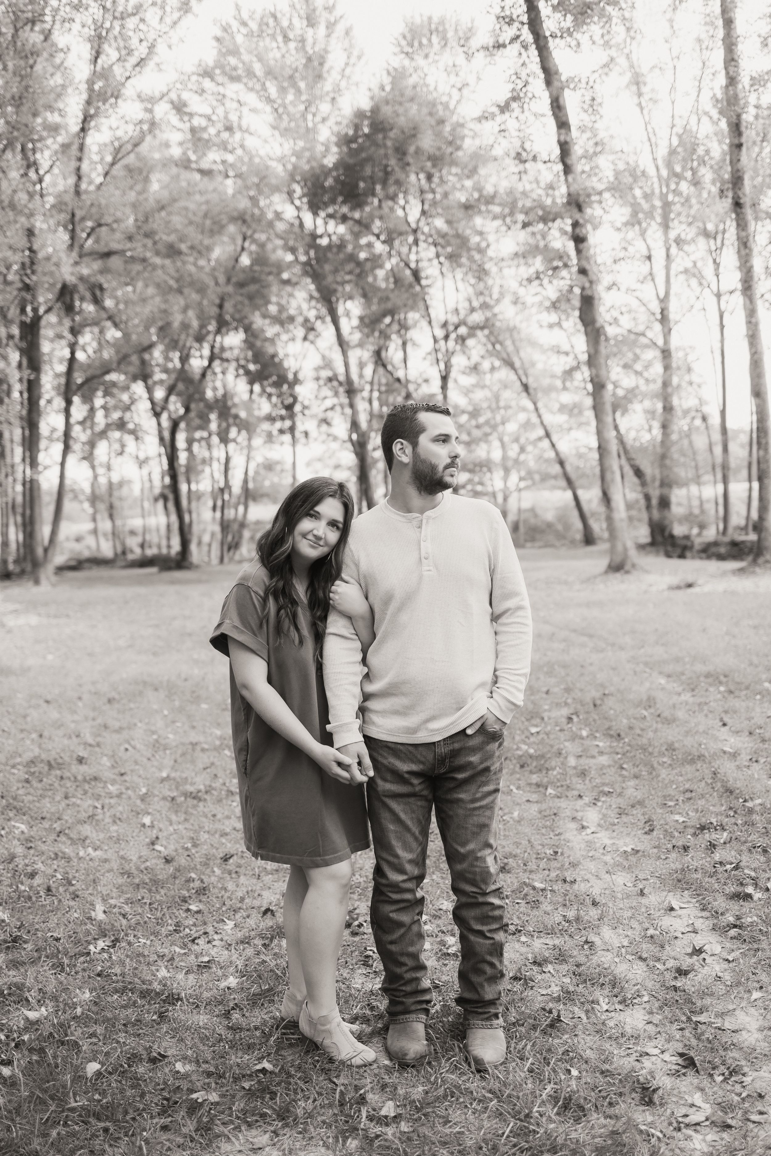 A couple shares tender moments in a wooded area during a black and white photo session.