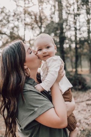 A loving parent holds and kisses their baby in a series of tender outdoor moments captured in natural lighting.