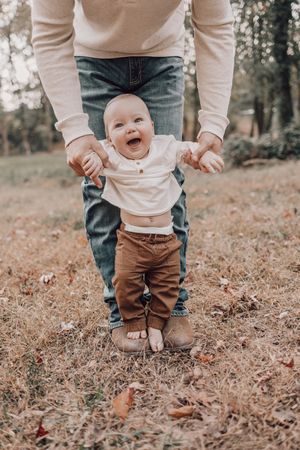 Small feet in brown pants stepping through fallen autumn leaves in a wooded setting.