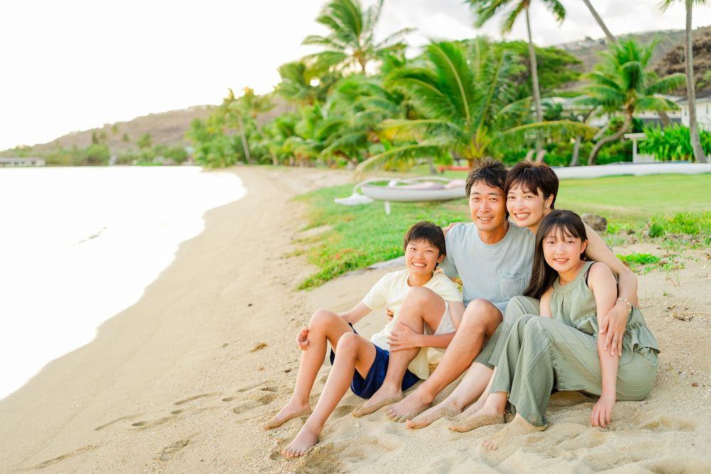 A group of people sitting together on a sandy beach with palm trees in the background during sunset.