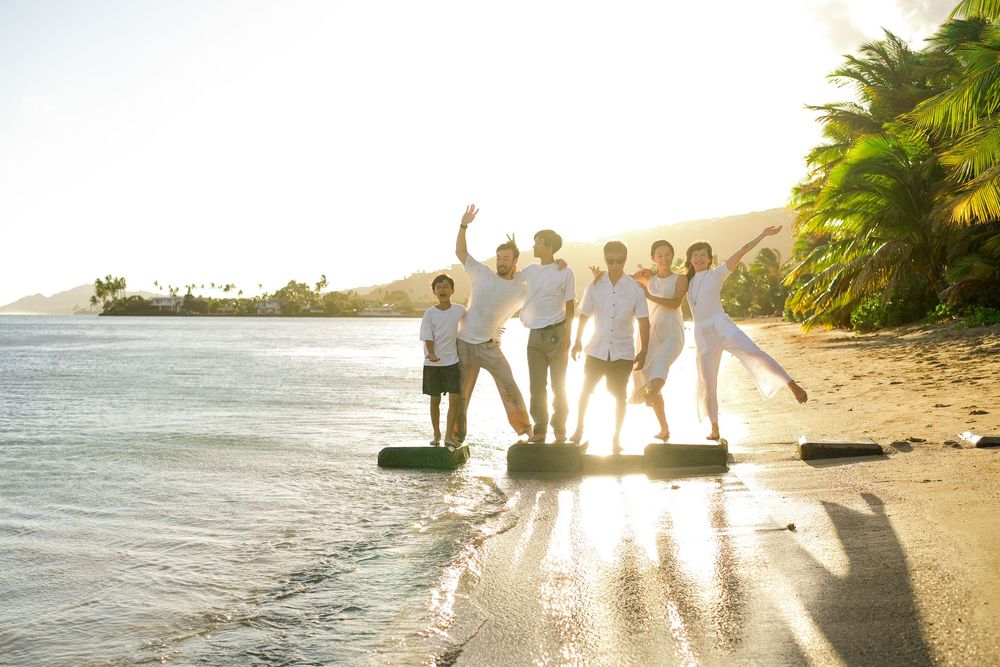 A group of people walking along a tropical beach at sunset with palm trees and golden light.