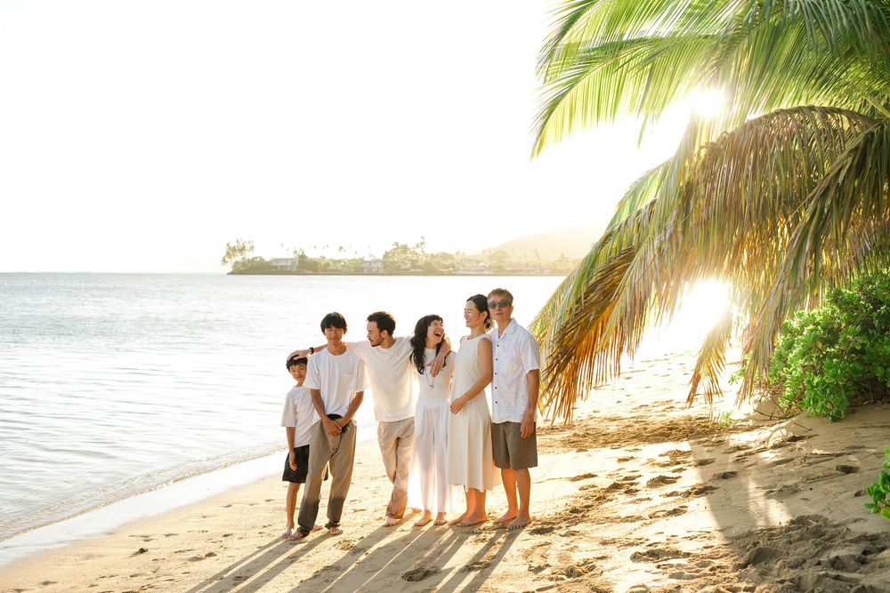 A group of people walking together on a tropical beach with palm trees and ocean views at sunset.