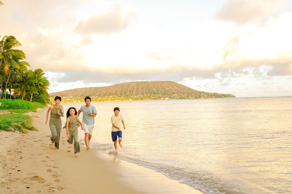 A group walks along a scenic Hawaiian beach with Diamond Head mountain in the background at sunset.