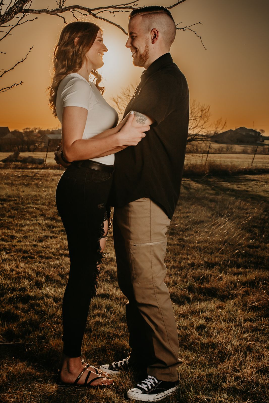 A couple poses intimately during a sunset photoshoot in a grassy field.