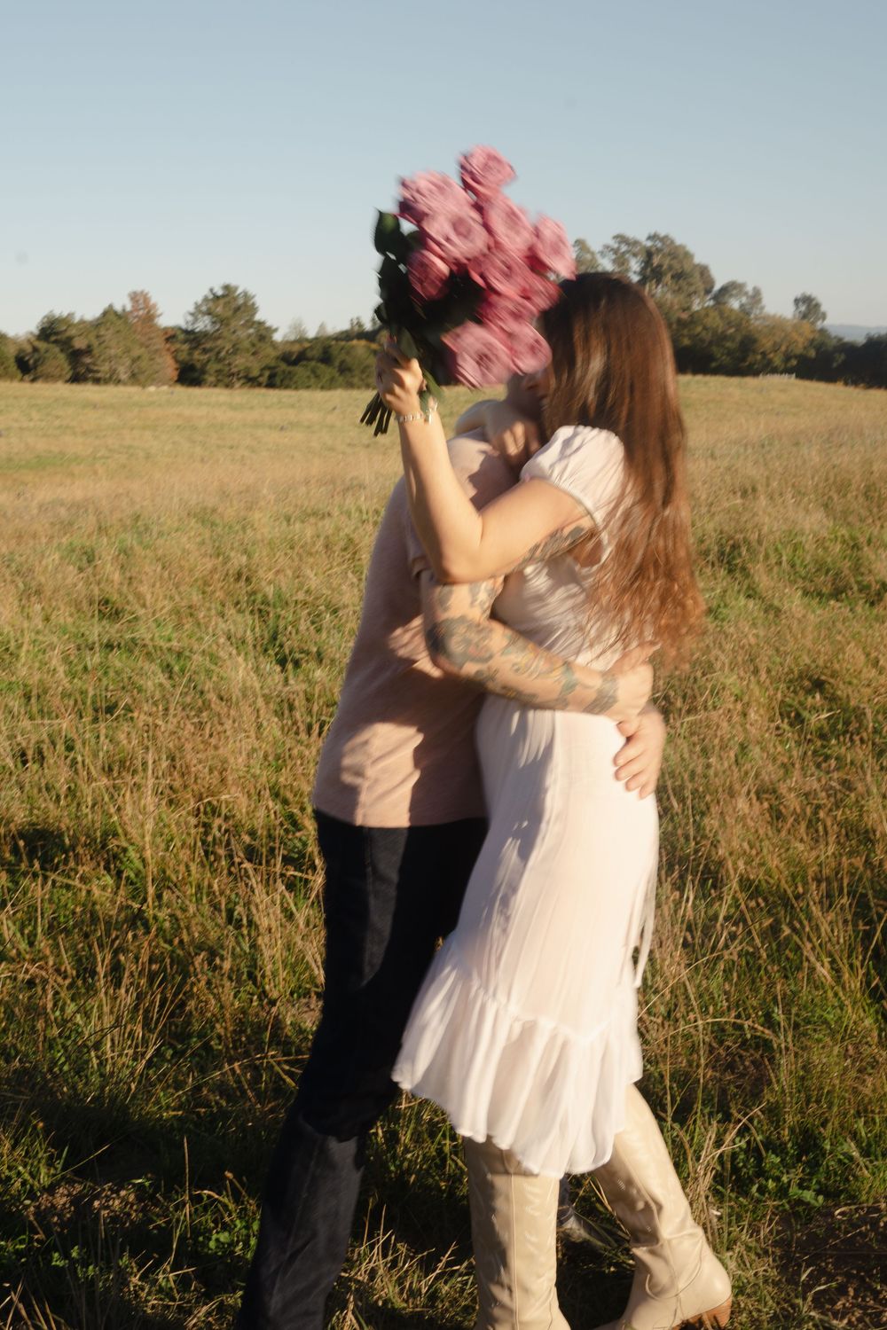 man and woman in the field hugging. she is holding pink roses, blurry picture