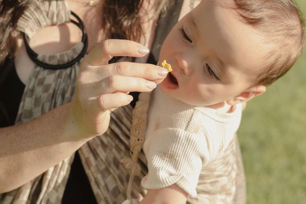 Mom holding baby in a sling smelling flowers