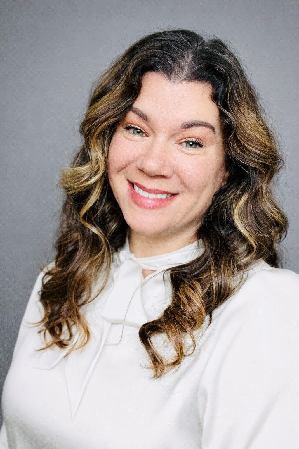 Professional headshot of someone in a black blazer against a blue backdrop.