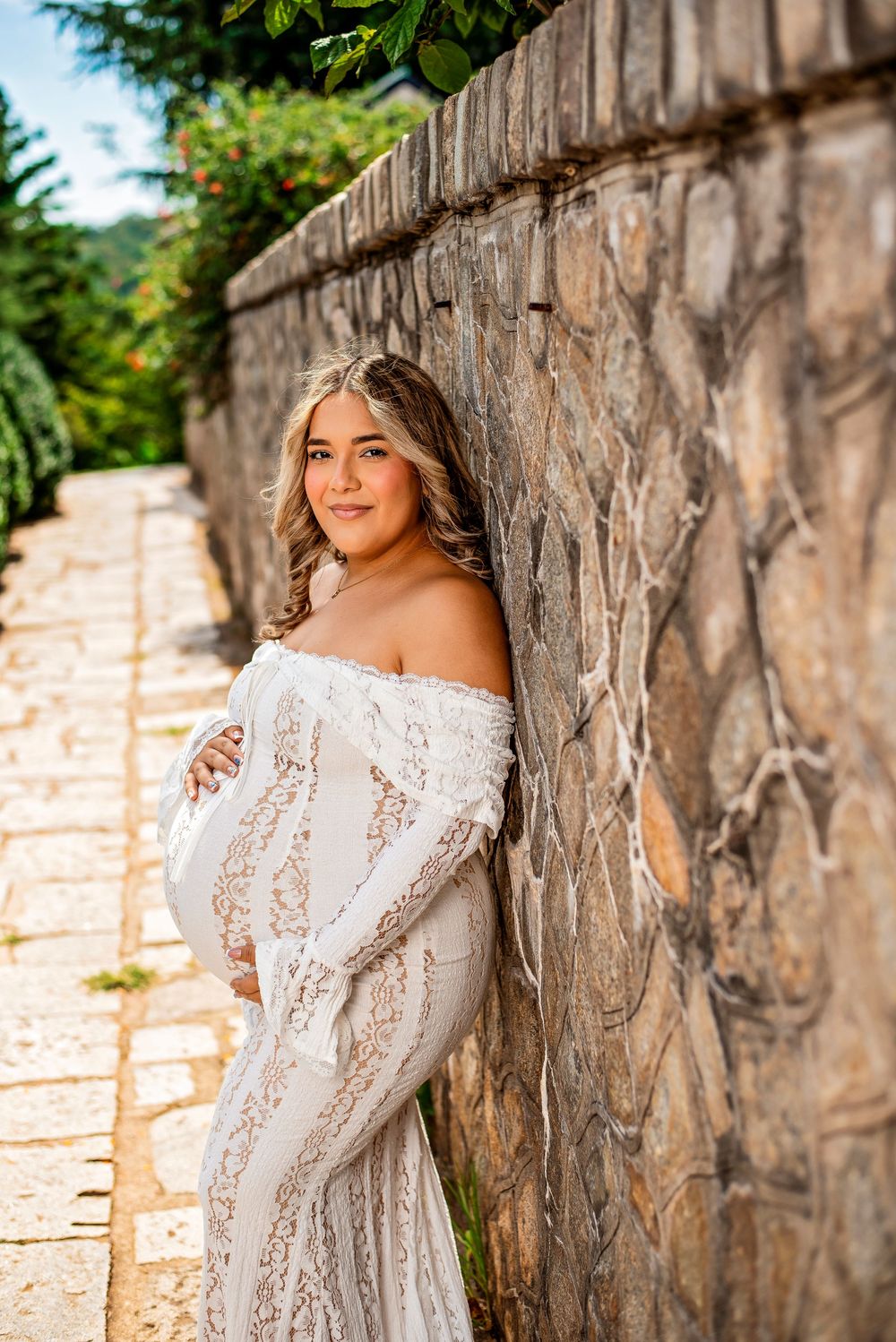 A person in a white lace dress poses against a rustic stone wall in an outdoor portrait session.
