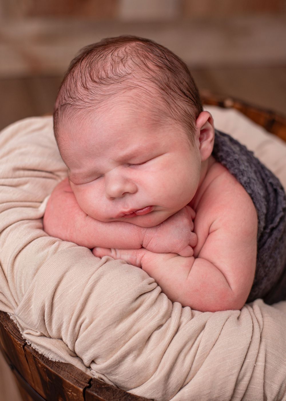 Sleeping newborn baby posed in a wooden bucket with cream fabric wrap for a professional newborn portrait.