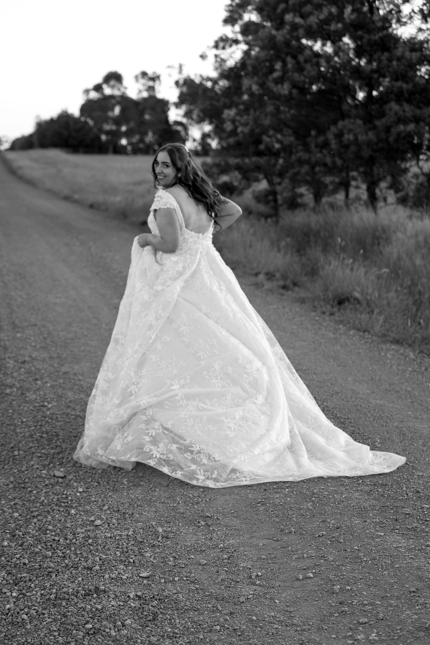 Black and white portrait of flowing white wedding dress movement on country road.