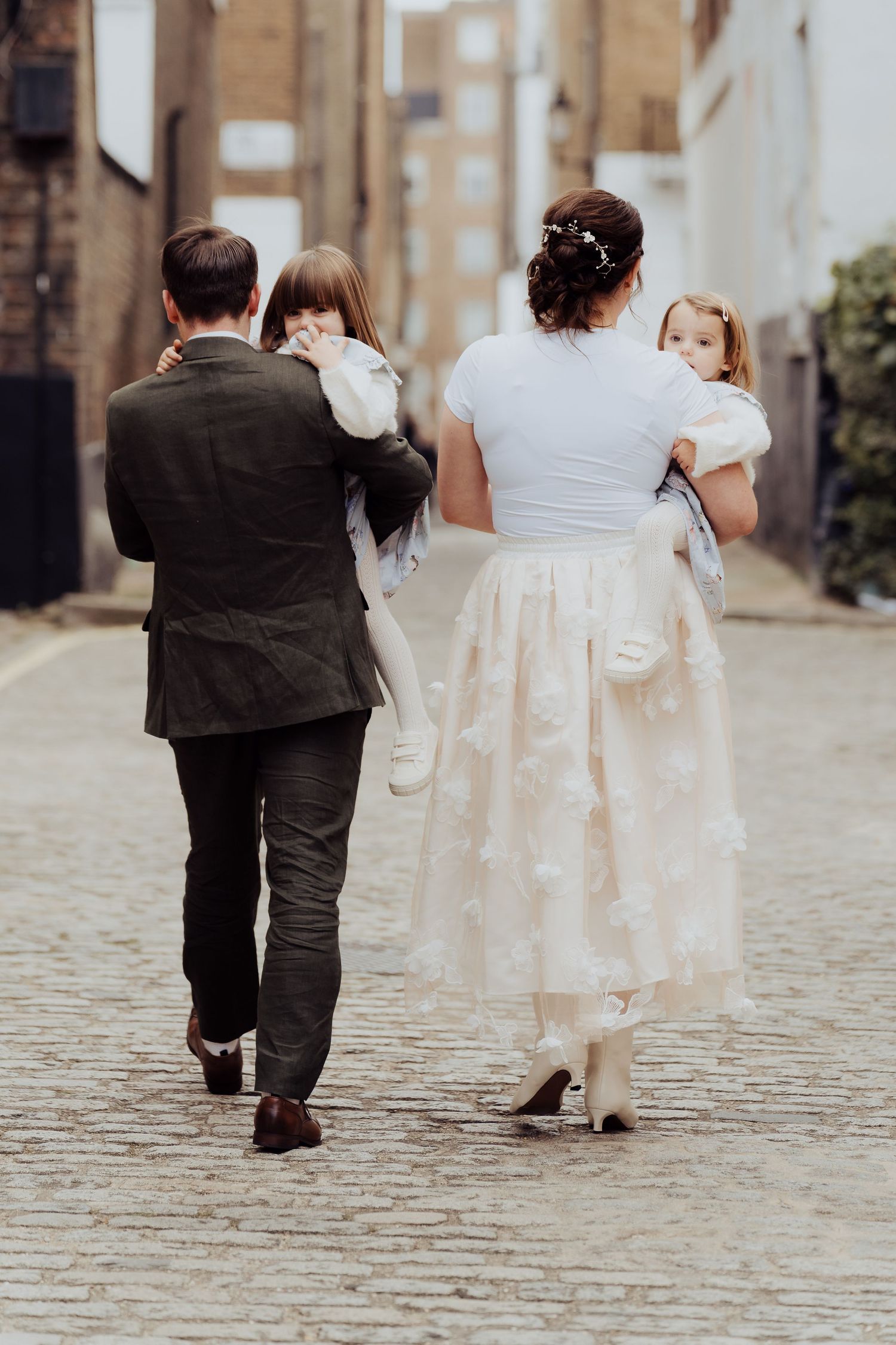 A couple in wedding attire walks away from camera on a cobblestone street in a series of candid photos.
