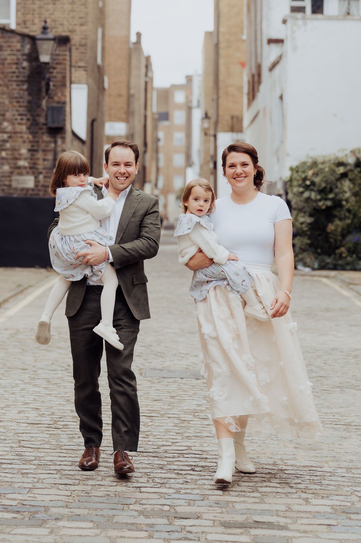 Couple in formal attire walking with baby on cobblestone street in five sequential photos showing their movement.