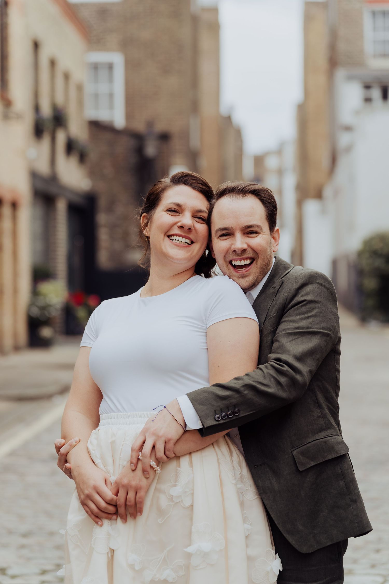 A joyful couple embraces and laughs together on a cobblestone street during their wedding photo session.