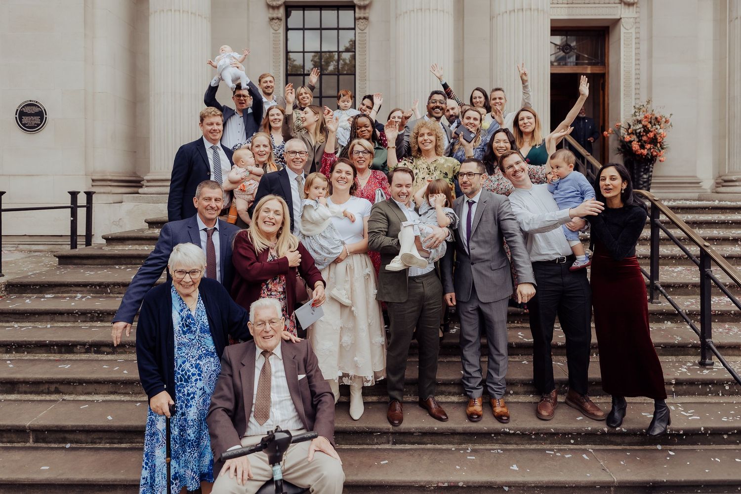 Wedding guests gather on stone steps outside a historic building for a group photograph.