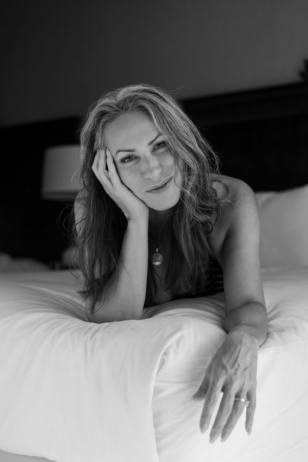 Black and white artistic photograph of a person lying on white bedding with dramatic shadows and lighting.