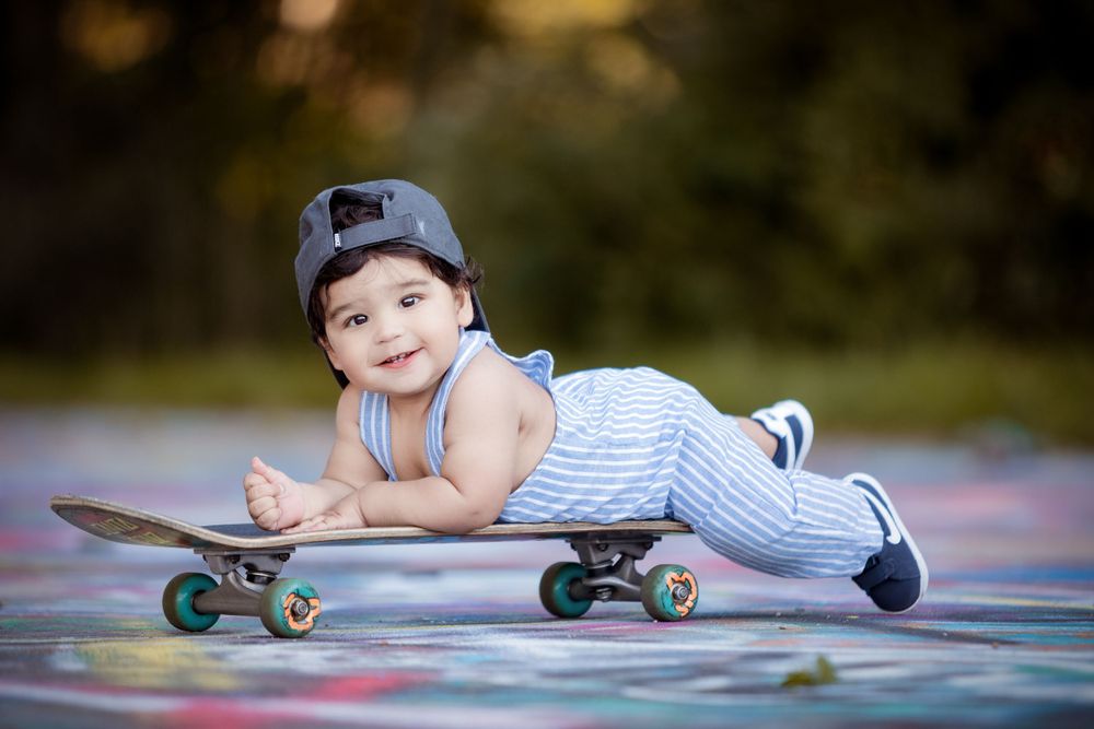 Baby in striped outfit lying on skateboard outdoors.