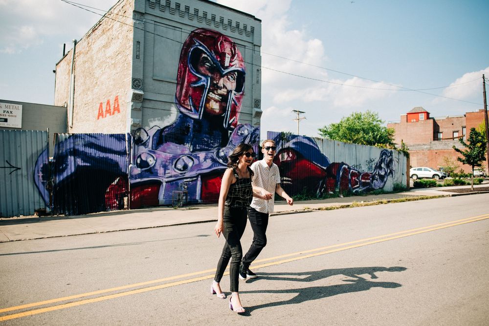 Someone skateboards down a street past colorful urban graffiti murals on a sunny day in a city setting.