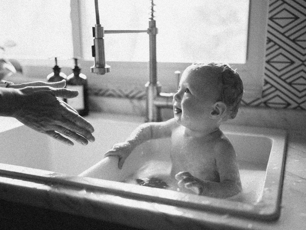 A baby getting a bath in a vintage kitchen sink in this nostalgic black and white photograph.
