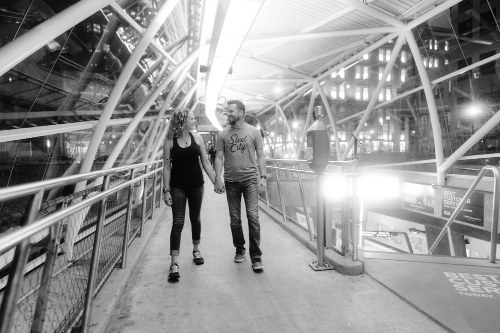 Monochromatic series of romantic couples walking through an industrial bridge or walkway structure.
