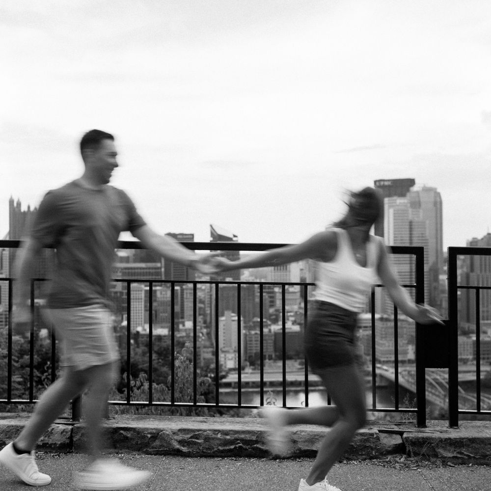 Motion sequence of couple running and jumping along waterfront railing with cityscape in background.