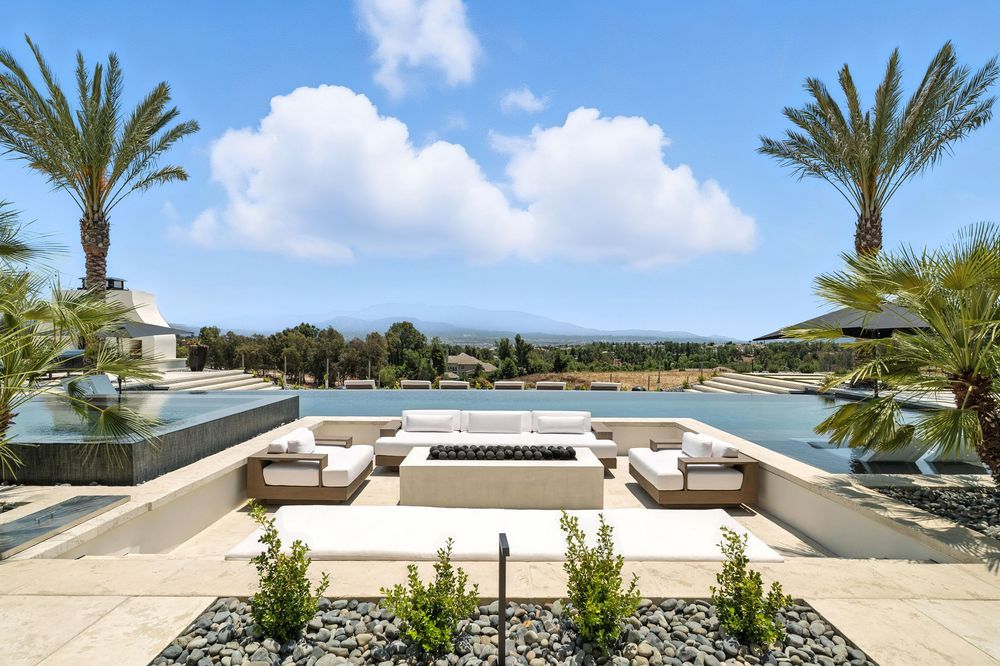 Modern white patio with lounge chairs, palm trees, and ocean views showcases a luxurious coastal living space.