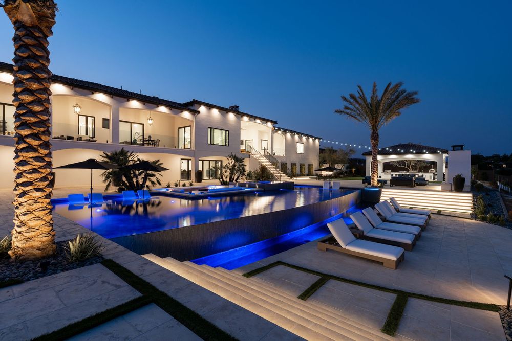Luxury poolside lounge area with illuminated blue lighting and palm trees at twilight creates an elegant resort atmosphere.
