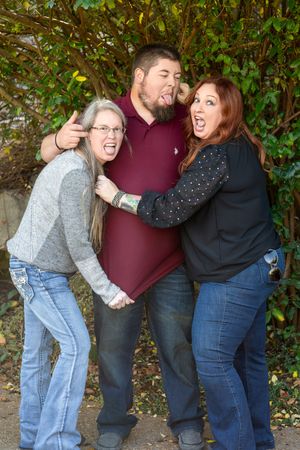 People laughing and posing playfully together in sequence against a leafy green backdrop in casual denim outfits.