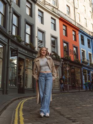 A person walks down a colorful cobblestone street wearing jeans and a beige coat.