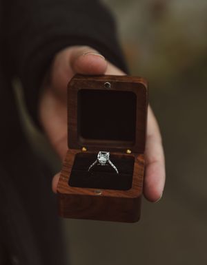 Small wooden ring box opening to reveal an engagement ring.