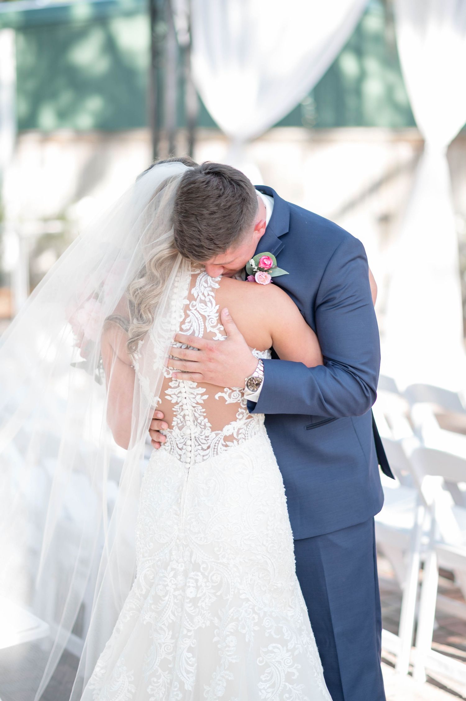 Romantic wedding moment captured with couple embracing under flowing white drapery.