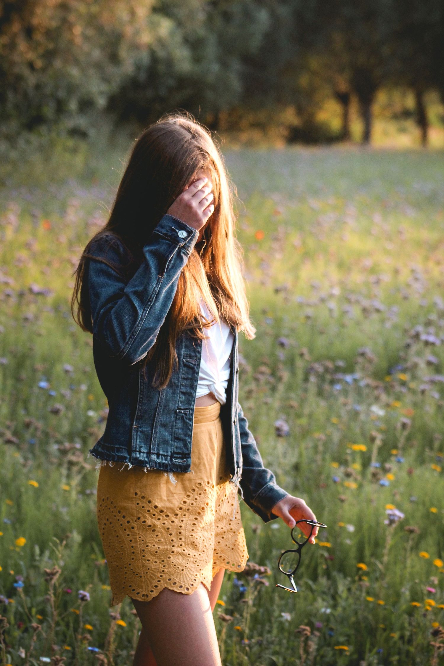 Girl standing in a field of flowers at sunset in Knokke, Belgium, golden hour, purple flowers, green grass, serene countryside scene.